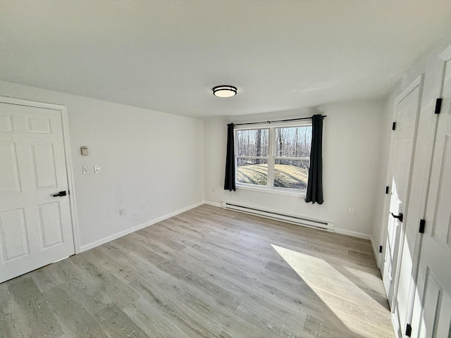 spare room featuring baseboard heating, light wood-style flooring, and baseboards