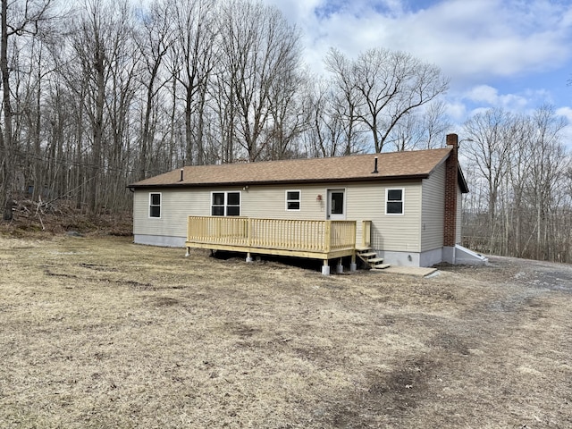 rear view of property with a deck, roof with shingles, and a chimney