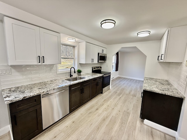 kitchen featuring light wood-type flooring, a sink, light stone counters, appliances with stainless steel finishes, and baseboards