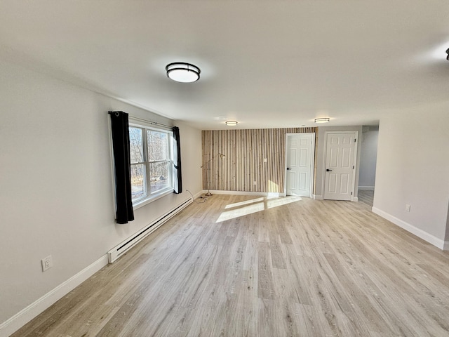 spare room featuring a baseboard heating unit, light wood-style floors, and baseboards