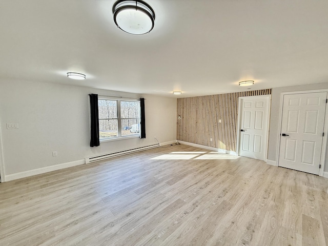 spare room with a baseboard heating unit, light wood-style floors, and baseboards