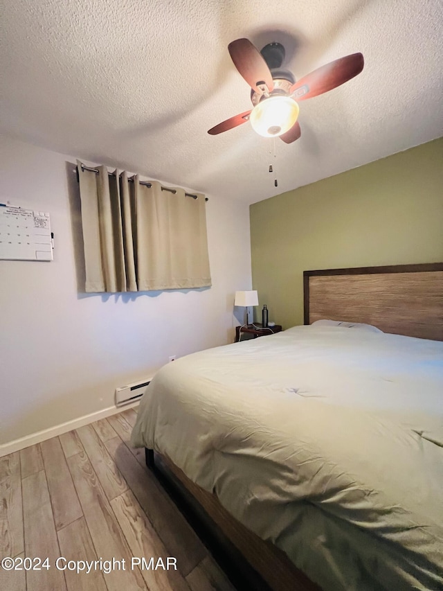 bedroom with a baseboard heating unit, a textured ceiling, wood finished floors, and baseboards