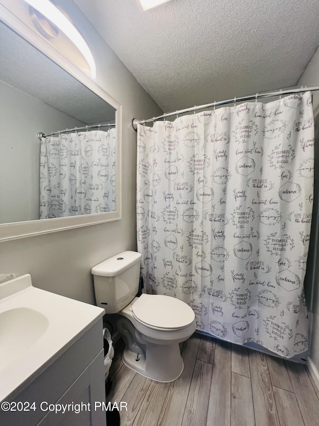 full bath with toilet, wood finished floors, curtained shower, a textured ceiling, and vanity