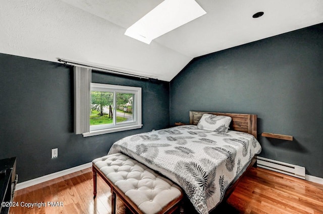 bedroom with a baseboard radiator, vaulted ceiling with skylight, baseboards, and wood finished floors