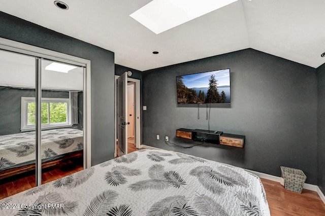 bedroom featuring vaulted ceiling with skylight, a closet, baseboards, and wood finished floors