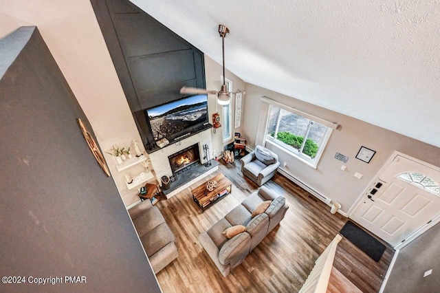 living area with a textured ceiling, a baseboard radiator, a fireplace, wood finished floors, and vaulted ceiling