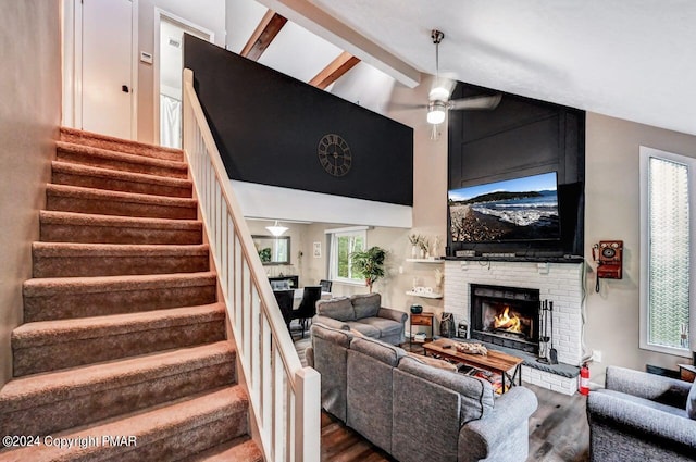 living area with beam ceiling, a ceiling fan, a brick fireplace, wood finished floors, and stairs