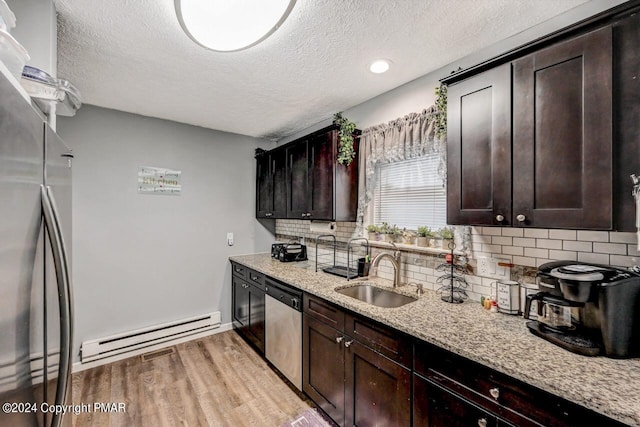 kitchen featuring light stone counters, a baseboard heating unit, stainless steel appliances, a sink, and light wood-type flooring