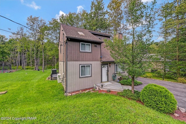 chalet / cabin featuring a shingled roof, a chimney, a front lawn, and aphalt driveway