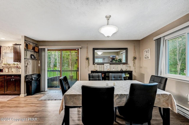 dining space featuring a baseboard heating unit, a textured ceiling, and light wood-type flooring