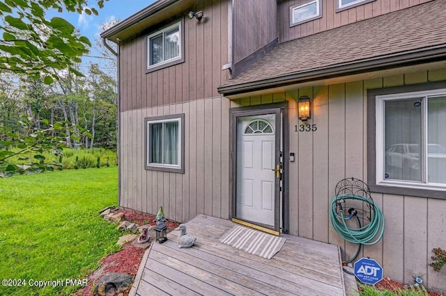 entrance to property featuring a yard and roof with shingles