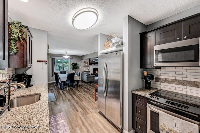 kitchen featuring appliances with stainless steel finishes, a lit fireplace, dark brown cabinets, light wood-style floors, and a sink