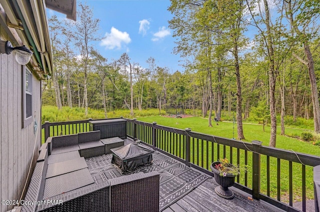 deck with a forest view, an outdoor living space with a fire pit, and a yard