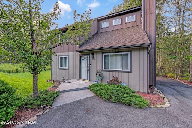 chalet / cabin with driveway, a shingled roof, and a front yard