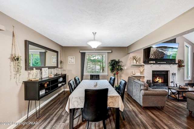 dining space with a textured ceiling, a brick fireplace, wood finished floors, and baseboards