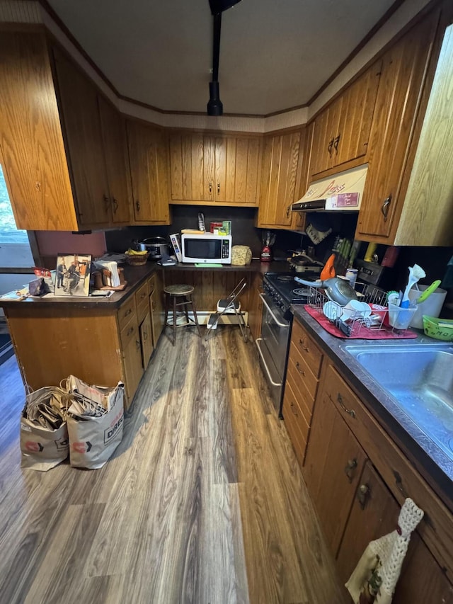 kitchen with brown cabinets, dark countertops, wood finished floors, white microwave, and under cabinet range hood