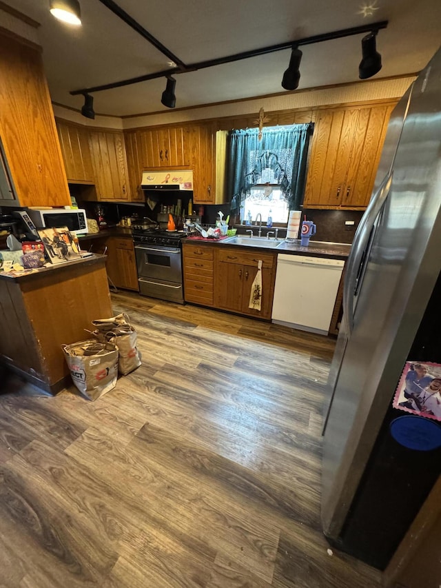 kitchen with track lighting, appliances with stainless steel finishes, brown cabinetry, and dark countertops