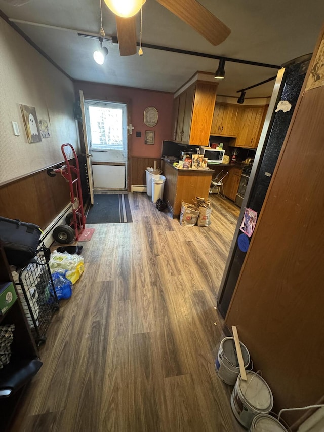kitchen featuring a peninsula, dark wood-type flooring, a wainscoted wall, brown cabinets, and rail lighting