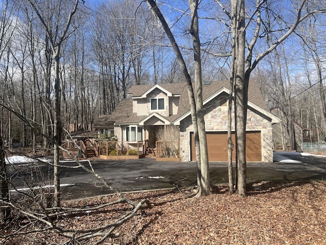 chalet / cabin featuring aphalt driveway, stone siding, a shingled roof, and a garage