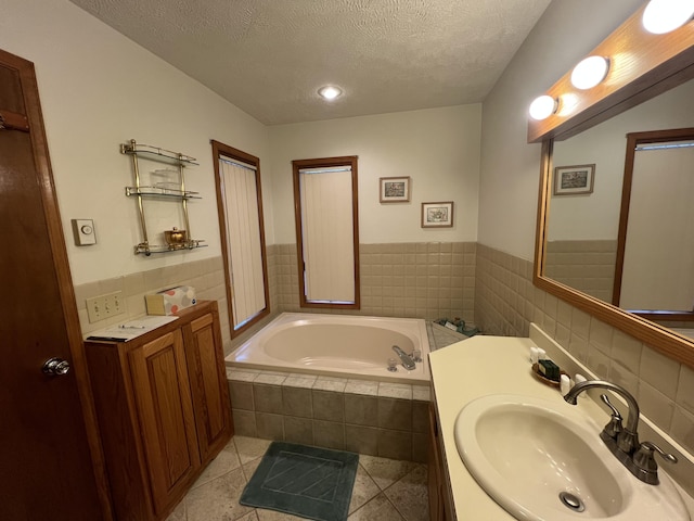 bathroom with a textured ceiling, tile patterned flooring, vanity, tile walls, and a bath