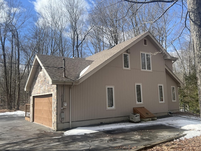 snow covered property featuring stone siding, a shingled roof, and an attached garage