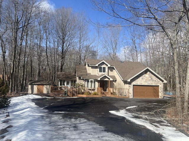 view of front of house with a deck, aphalt driveway, an attached garage, a shingled roof, and stone siding