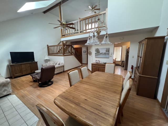 dining room with a skylight, beam ceiling, light wood finished floors, stairway, and high vaulted ceiling