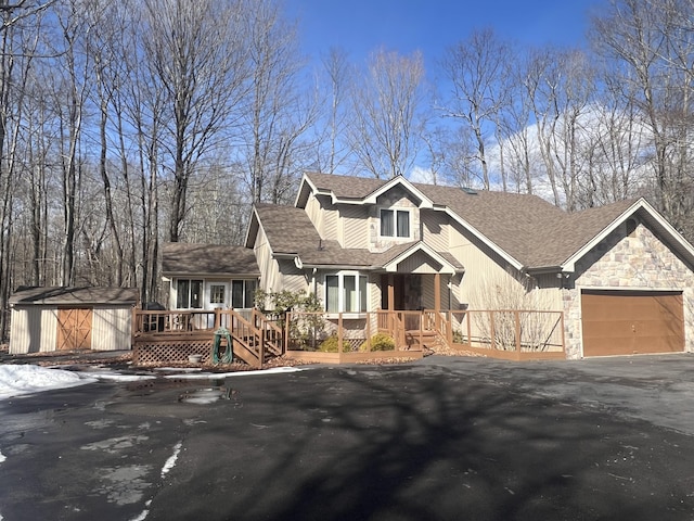 rustic home with a garage, a storage shed, stone siding, aphalt driveway, and an outdoor structure