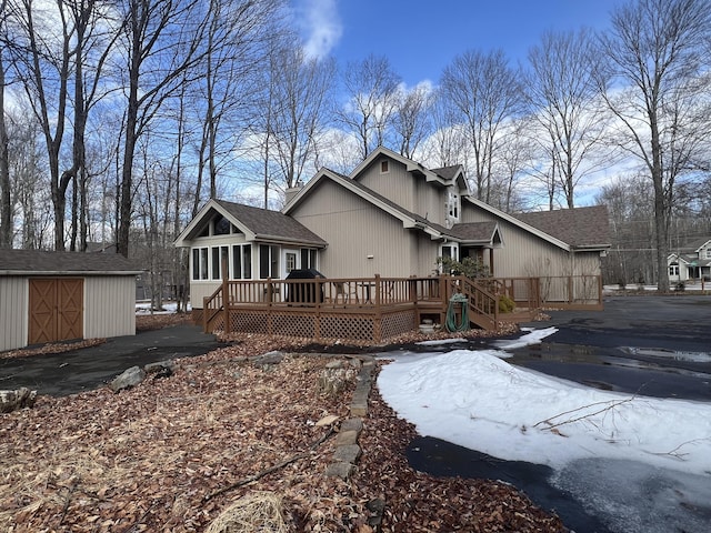 back of property with an outbuilding, a storage shed, a deck, and roof with shingles