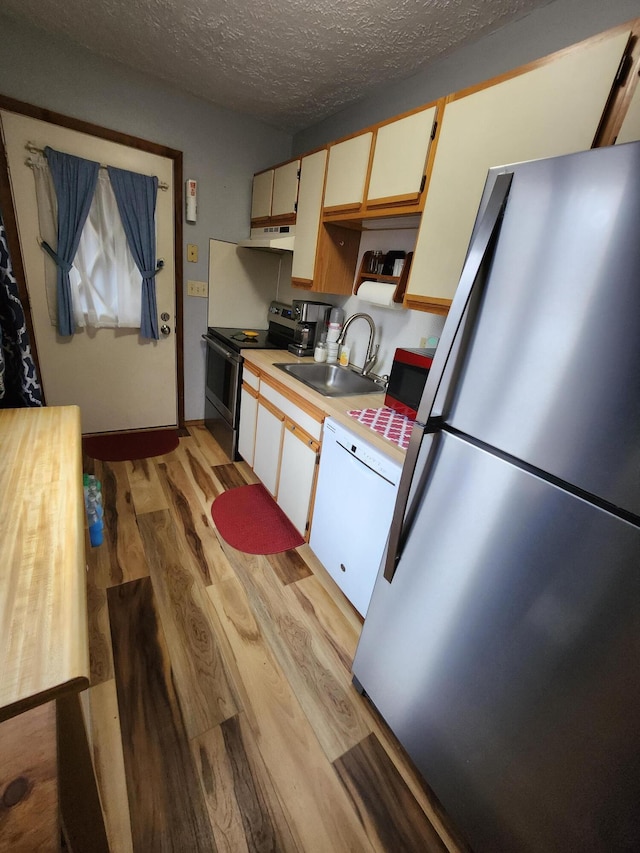 kitchen with light wood finished floors, under cabinet range hood, a sink, a textured ceiling, and appliances with stainless steel finishes