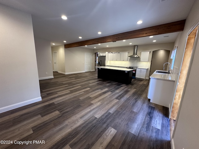kitchen featuring wall chimney range hood, a sink, beam ceiling, and appliances with stainless steel finishes