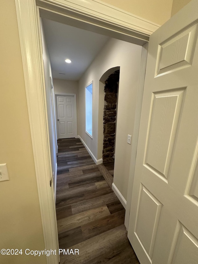 corridor featuring baseboards, arched walkways, and dark wood-style flooring