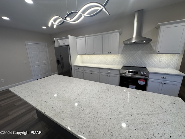 kitchen with baseboards, light stone countertops, wall chimney exhaust hood, stainless steel appliances, and backsplash