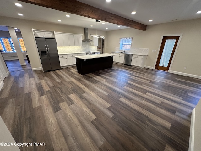 kitchen with light countertops, wall chimney exhaust hood, stainless steel appliances, beam ceiling, and backsplash