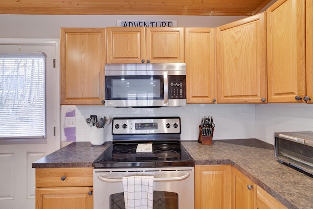 kitchen with stainless steel appliances, dark countertops, light brown cabinets, and decorative backsplash