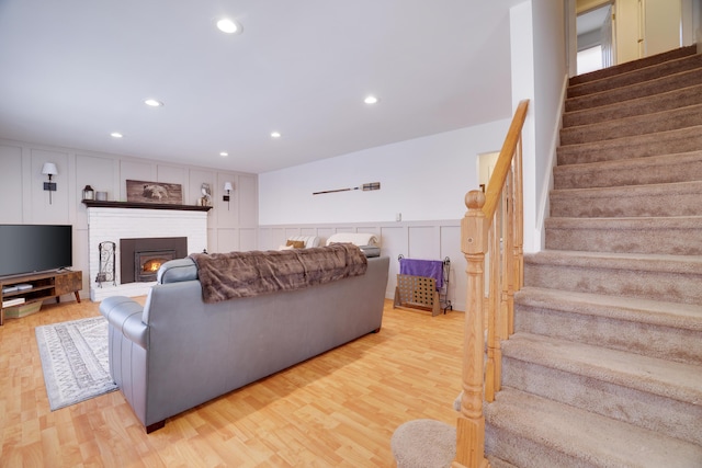 living room with light wood-style flooring, stairs, a fireplace, and wainscoting