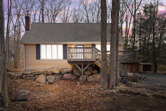 view of front of property featuring stairs, a chimney, a deck, and roof with shingles