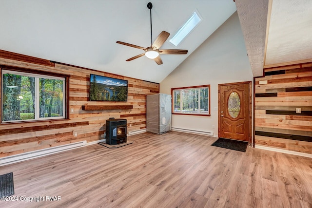 unfurnished living room with a wood stove, wooden walls, a wealth of natural light, and a baseboard radiator