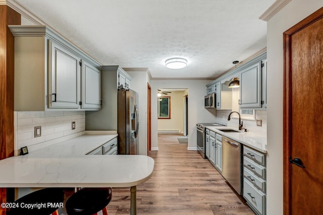 kitchen with crown molding, appliances with stainless steel finishes, a peninsula, light wood-style floors, and a sink