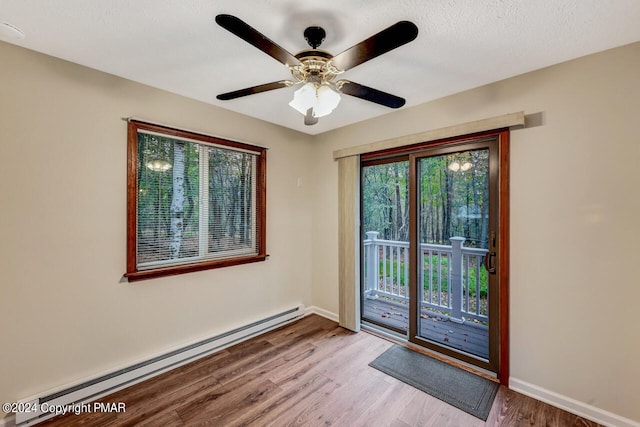 doorway featuring baseboards, baseboard heating, wood finished floors, a textured ceiling, and a ceiling fan