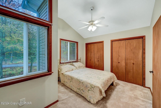 bedroom with light carpet, a ceiling fan, multiple closets, and vaulted ceiling