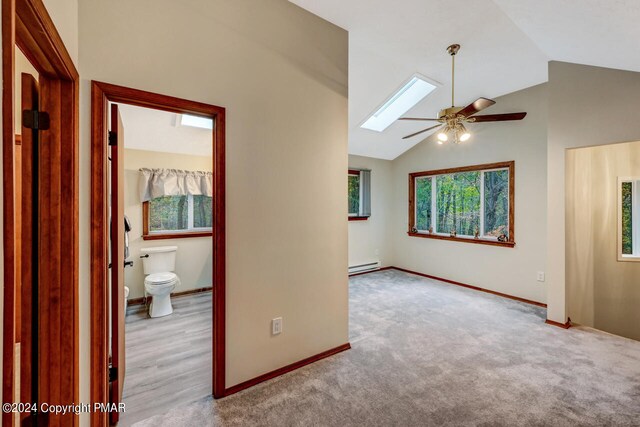 carpeted spare room featuring vaulted ceiling with skylight, baseboards, a baseboard heating unit, and a ceiling fan