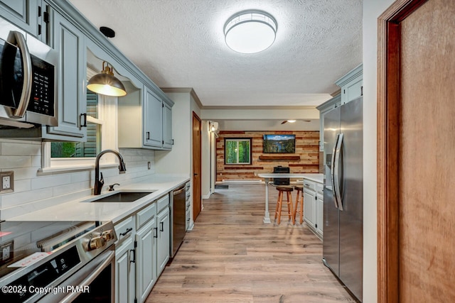 kitchen featuring a sink, light countertops, light wood-style floors, appliances with stainless steel finishes, and tasteful backsplash