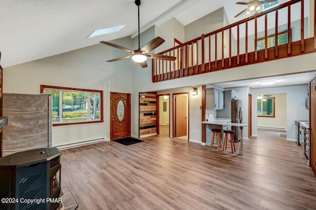 unfurnished living room featuring baseboards, a wood stove, wood finished floors, a ceiling fan, and a baseboard radiator