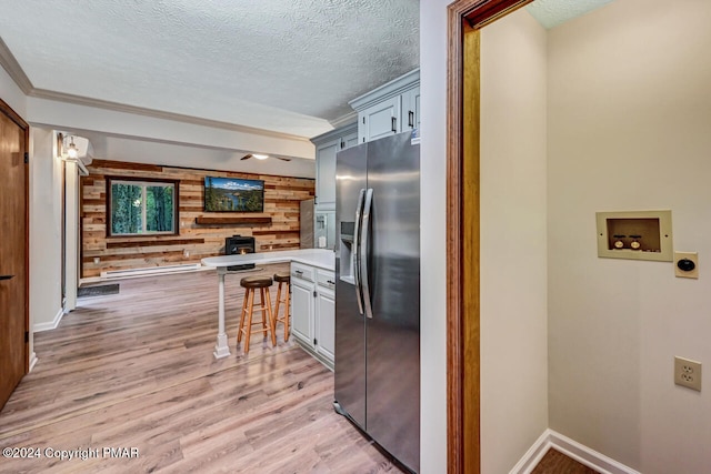 kitchen with a kitchen bar, light wood-style flooring, a textured ceiling, wooden walls, and stainless steel fridge with ice dispenser