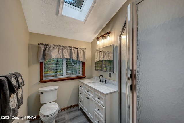 bathroom featuring baseboards, lofted ceiling with skylight, vanity, wood finished floors, and a textured ceiling