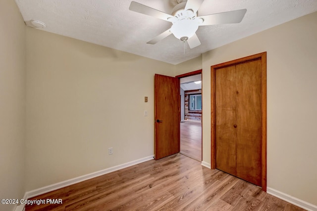 unfurnished bedroom featuring light wood-style flooring, a ceiling fan, a textured ceiling, a closet, and baseboards