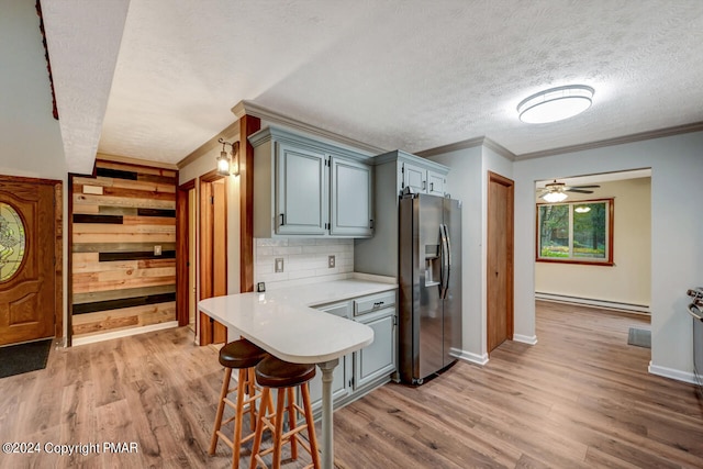 kitchen with a breakfast bar, stainless steel fridge, light wood-style floors, light countertops, and baseboard heating