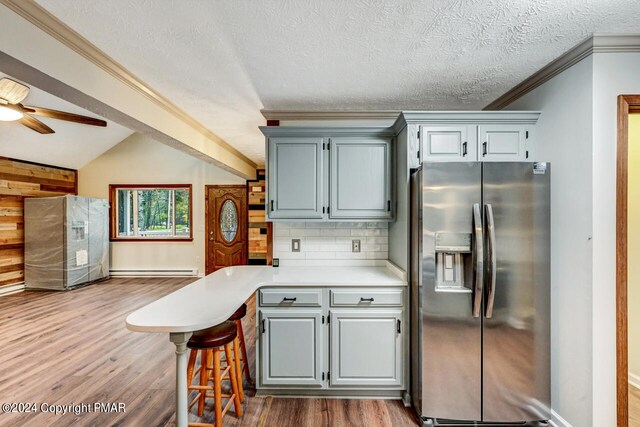 kitchen featuring wood finished floors, a peninsula, stainless steel fridge with ice dispenser, light countertops, and vaulted ceiling