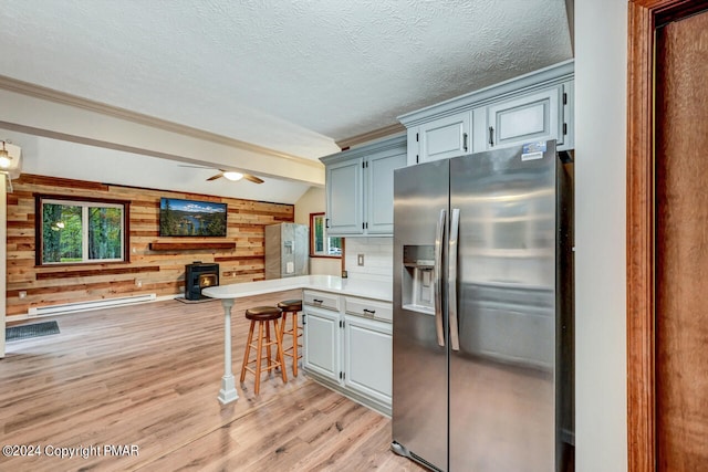 kitchen with light wood finished floors, a peninsula, a wood stove, stainless steel fridge with ice dispenser, and a kitchen bar